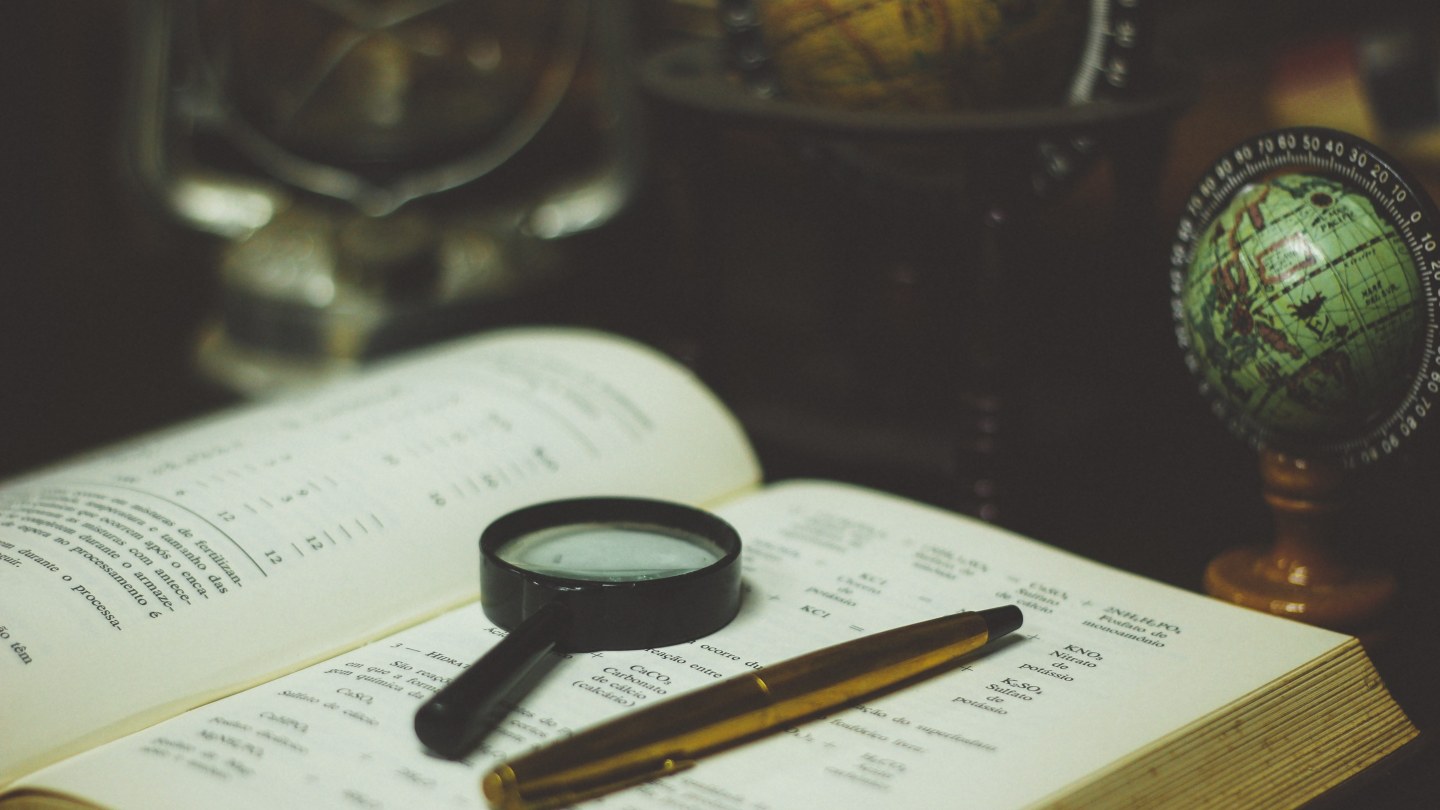 Loupe pos&eacute;e sur un livre ouvert &agrave; c&ocirc;t&eacute; d'un globe